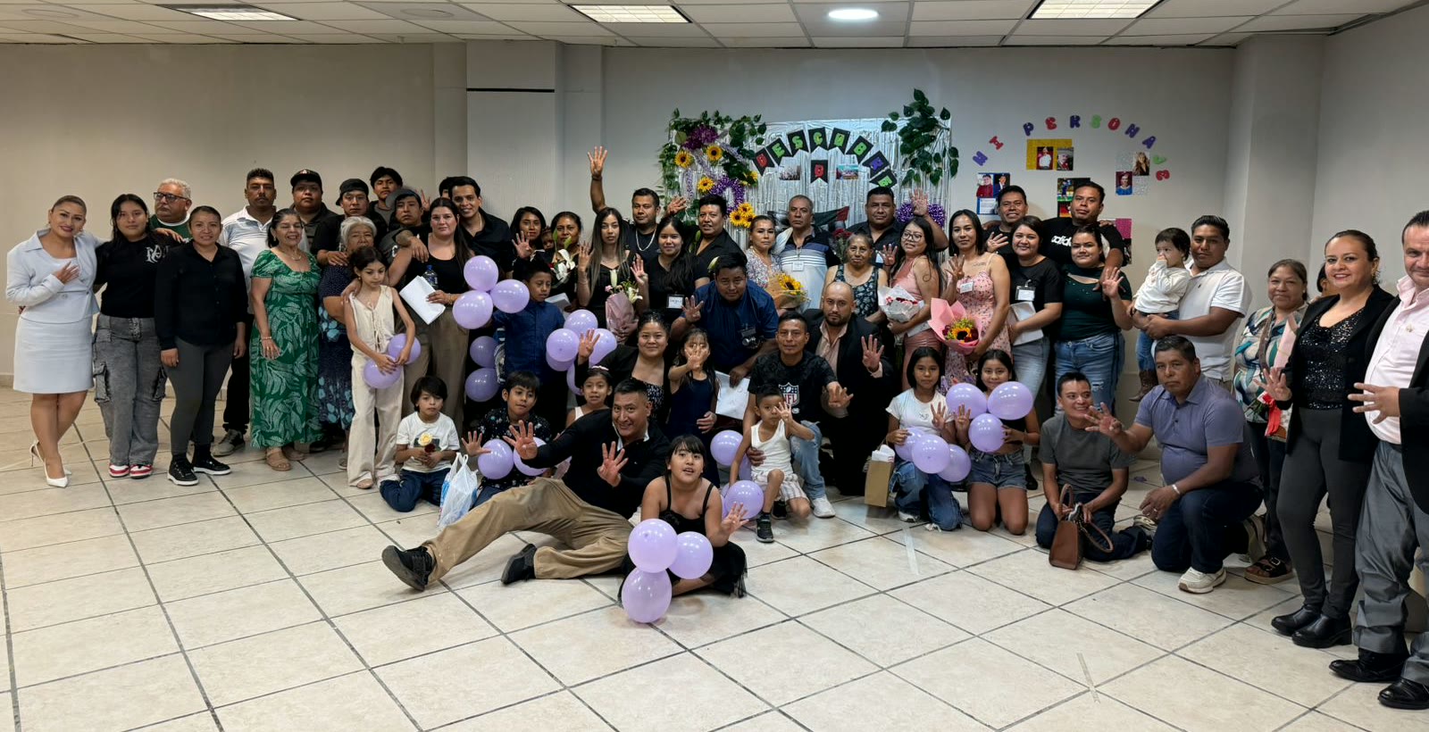 Fotografía de grupo al cerrar un programa de Kairos en Guadalajara: unas cincuenta personas, familias completas, sonriendo con globos y flores.